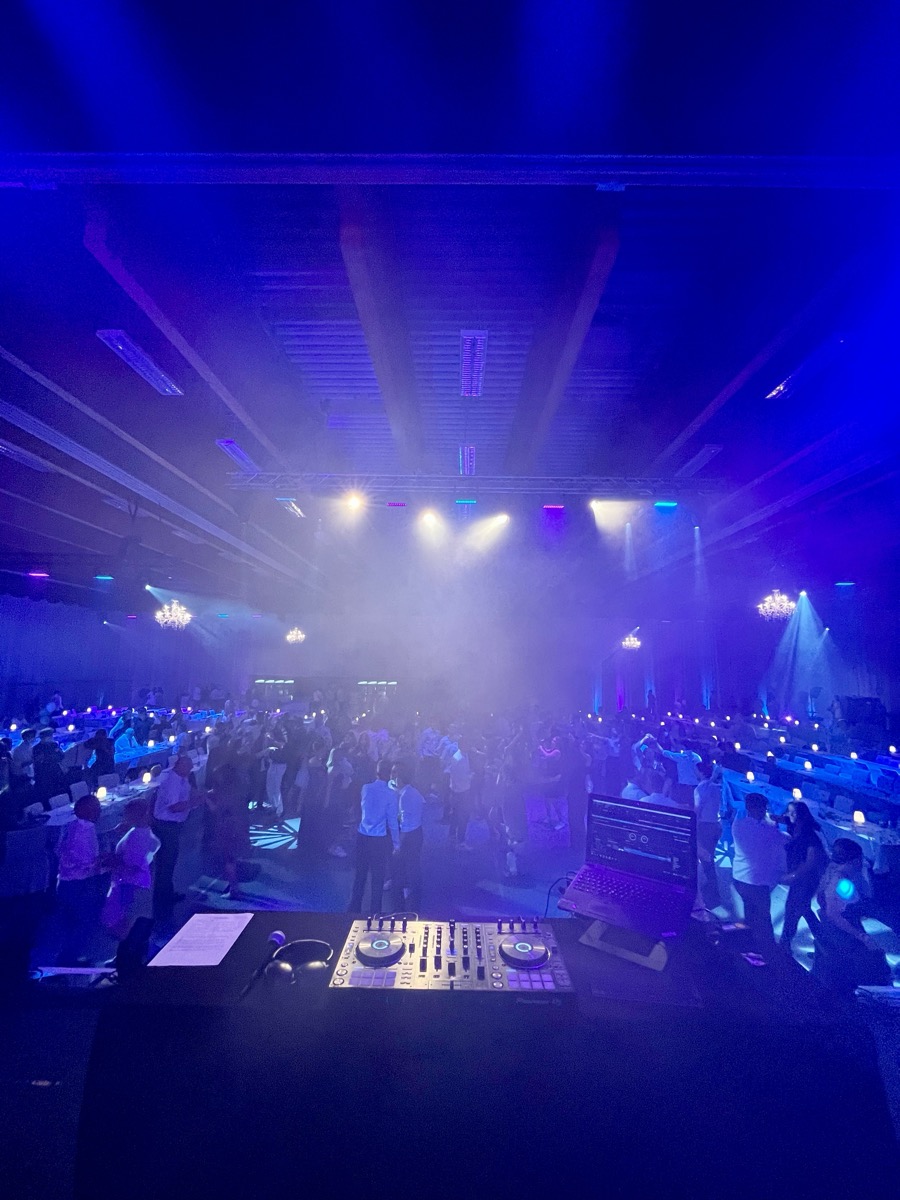 DJ-Pult vor einer großen Halle mit Lichtshow
